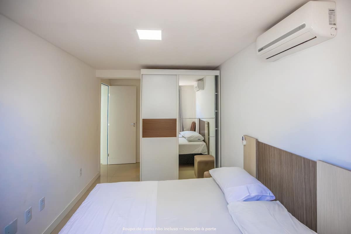 A hotel room with a bed, an air conditioning unit, a wardrobe, and a bathroom visible through an open door.
