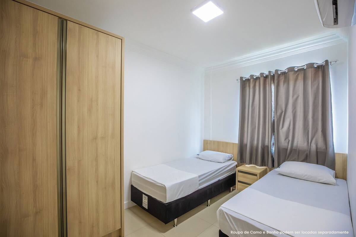 A bedroom with two single beds, a wooden wardrobe, and a nightstand.