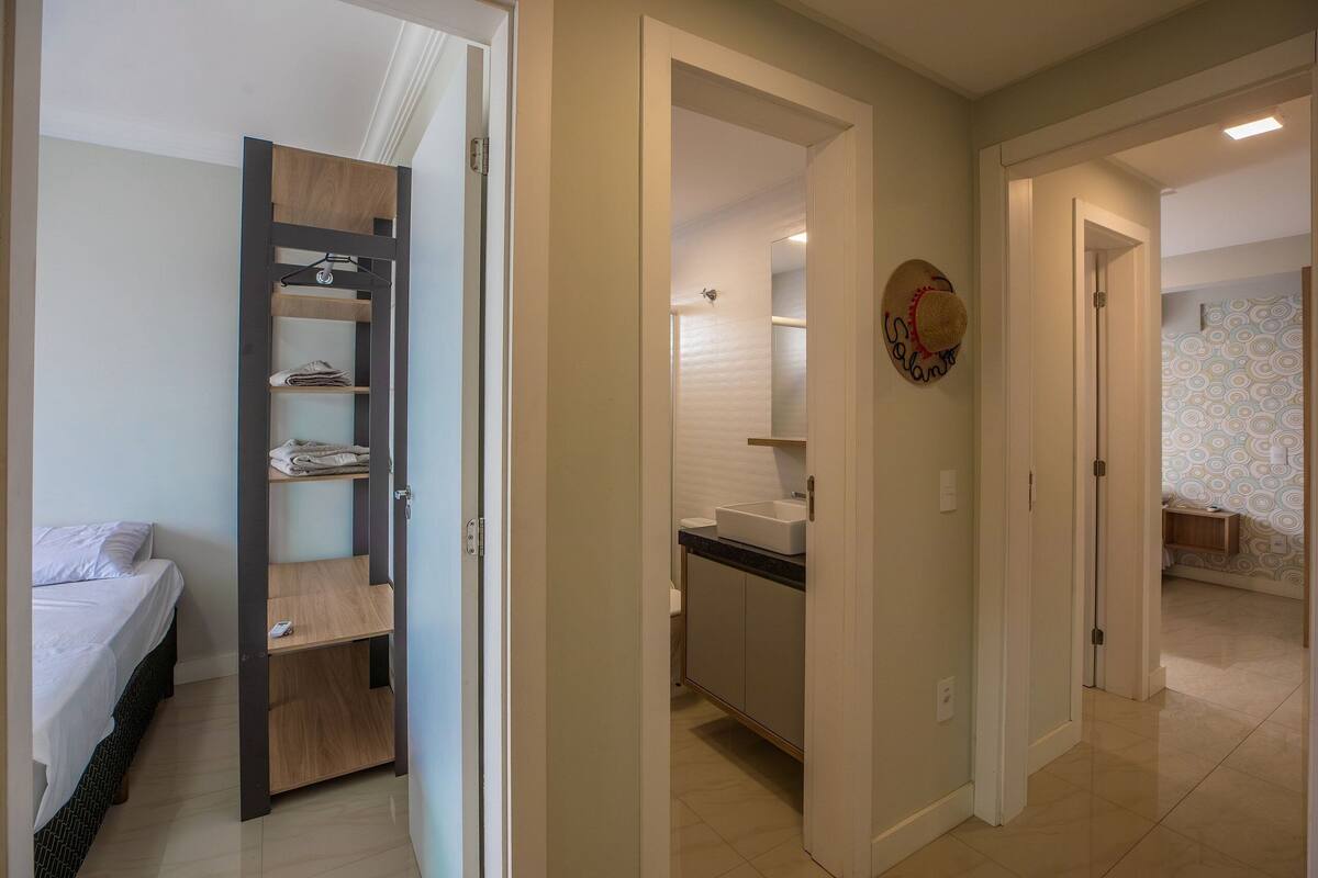 A bedroom with a bed, a wooden shelf unit, and a bathroom with a sink and mirror.