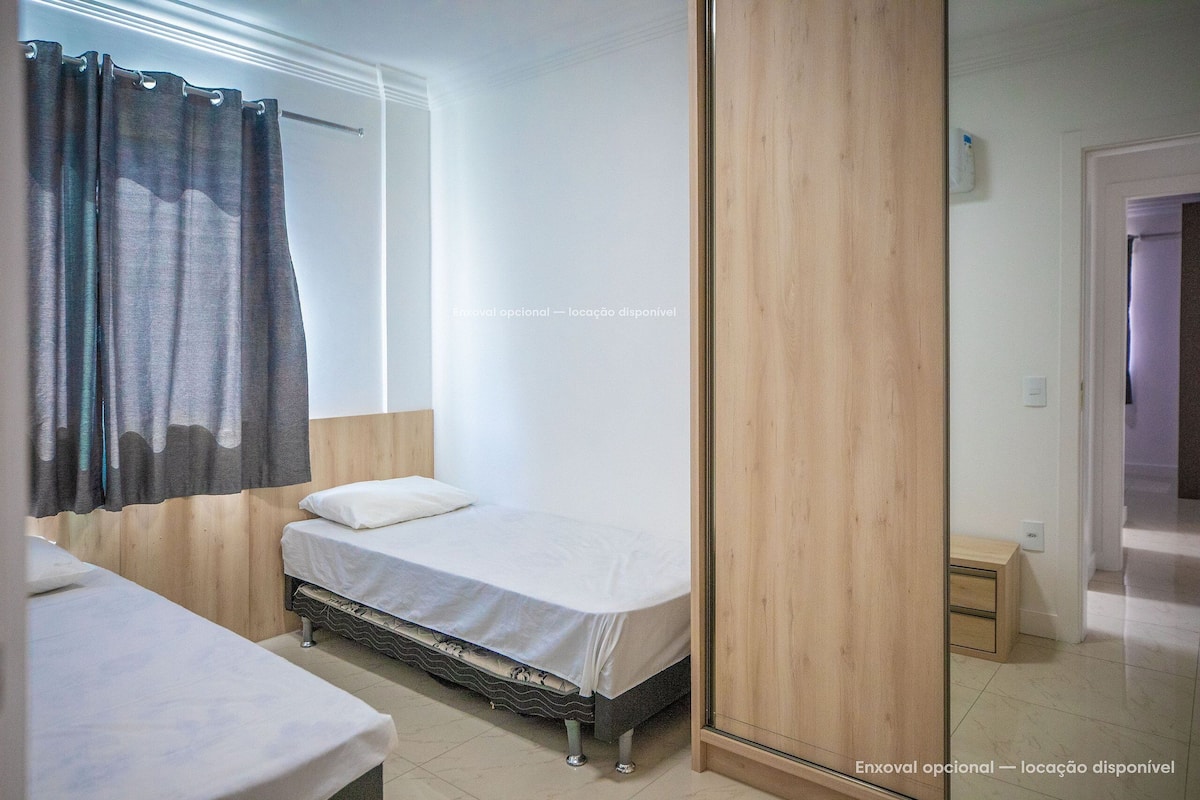 A bedroom with two beds, a wooden wardrobe, and a bathroom visible in the background.