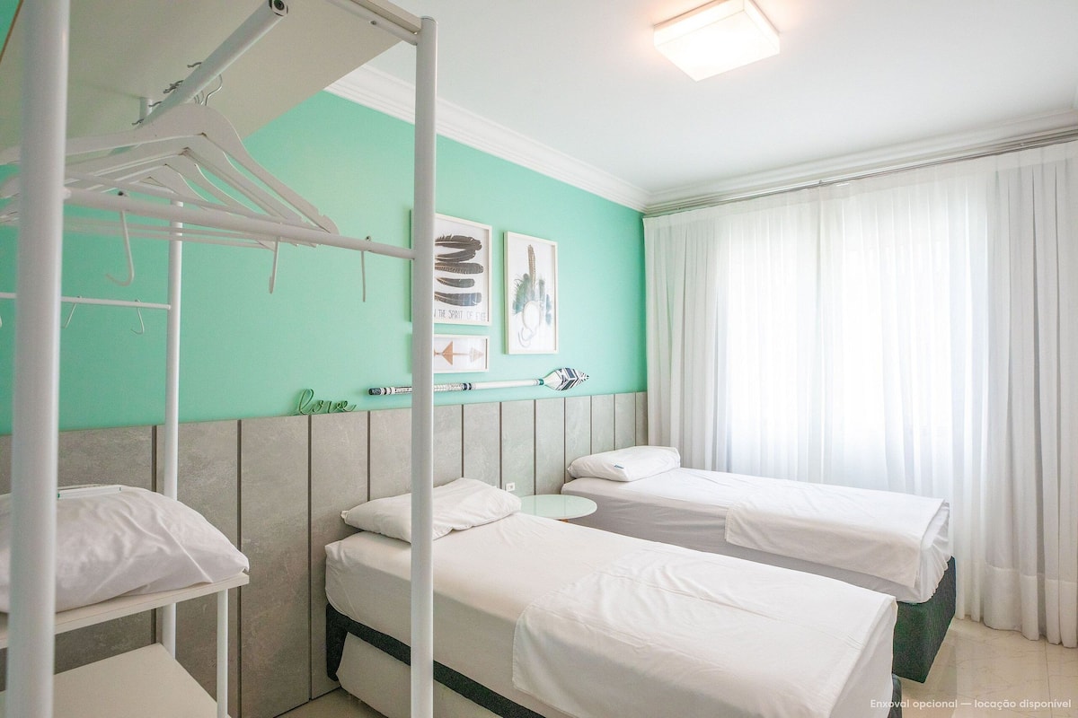 A hotel room with two beds, a bunk bed, a white wardrobe, a small round table, and a window with curtains.