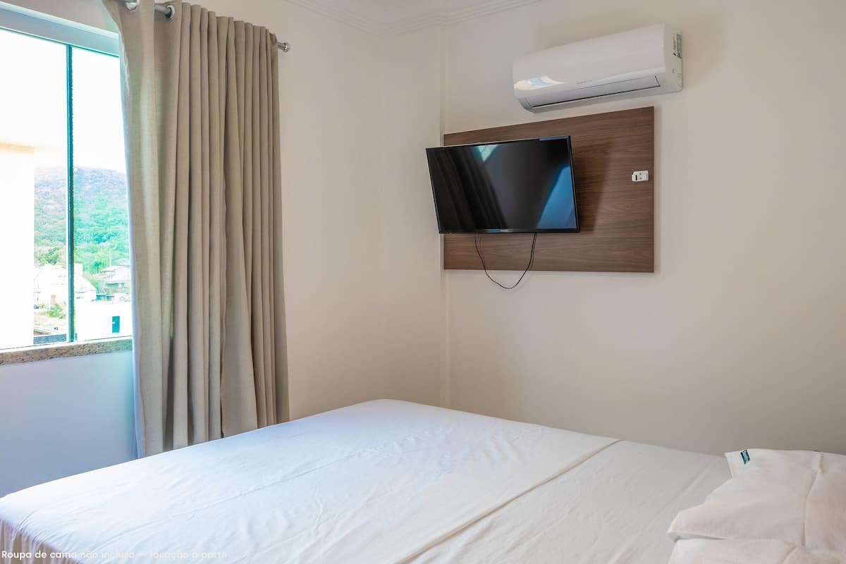 A hotel room with a bed, a TV mounted on the wall, and an air conditioning unit.