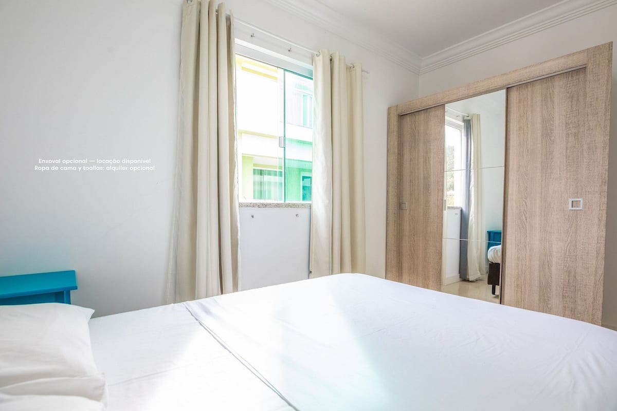 A hotel room with a bed, a window with curtains, and a wooden wardrobe.