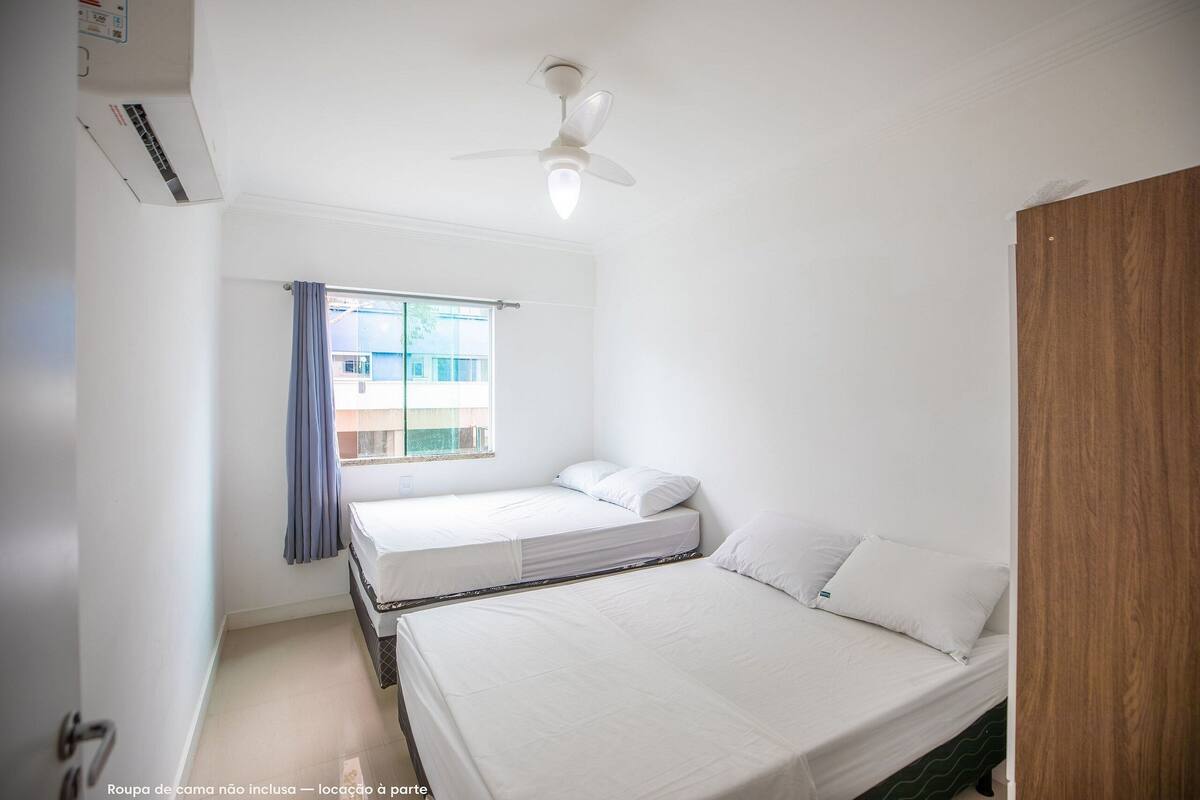 A room with two single beds, a ceiling fan, and a window with curtains.