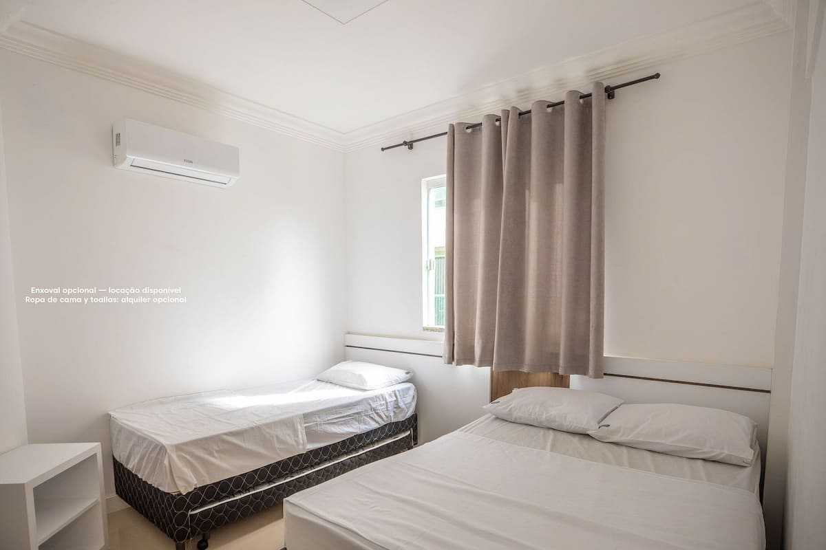 A bedroom with two beds, a window with curtains, and a wall-mounted air conditioner.