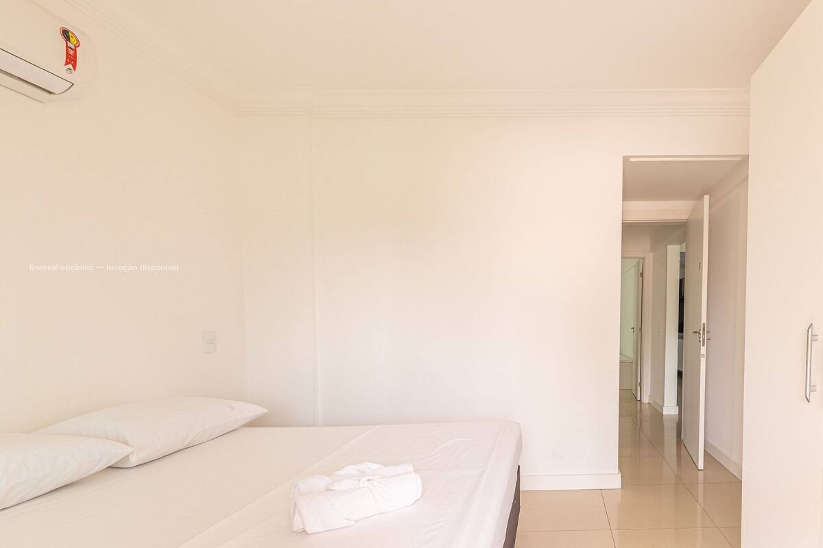 A hotel room with a neatly made bed, a visible door, and a hallway leading to other rooms.