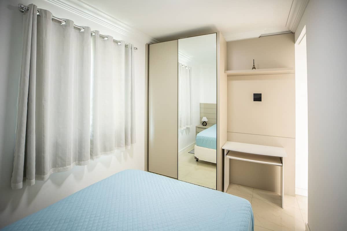 A bedroom with a bed, a mirror, a bedside table, and a nightstand.