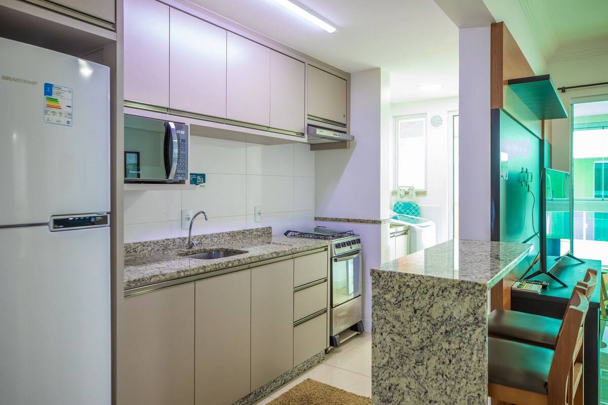 A modern kitchen with a built-in microwave, oven, and sink. There is a dining area with a bar counter and chairs.