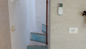 En trappa med blåa steg som leder upp till en liten plattform, en väggmonterad intercom och ett eluttag.