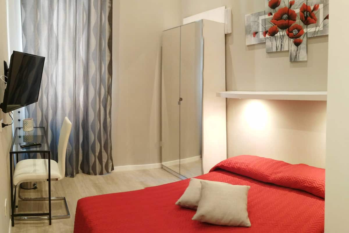 Ein Hotelzimmer mit Bett, Fernseher, Stuhl, Dusche und einem Wandbild.