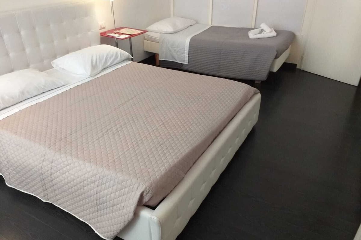 Ein Hotelzimmer mit einem großen Bett, einem kleineren Bett, einem Nachttisch und einem Beistelltisch.