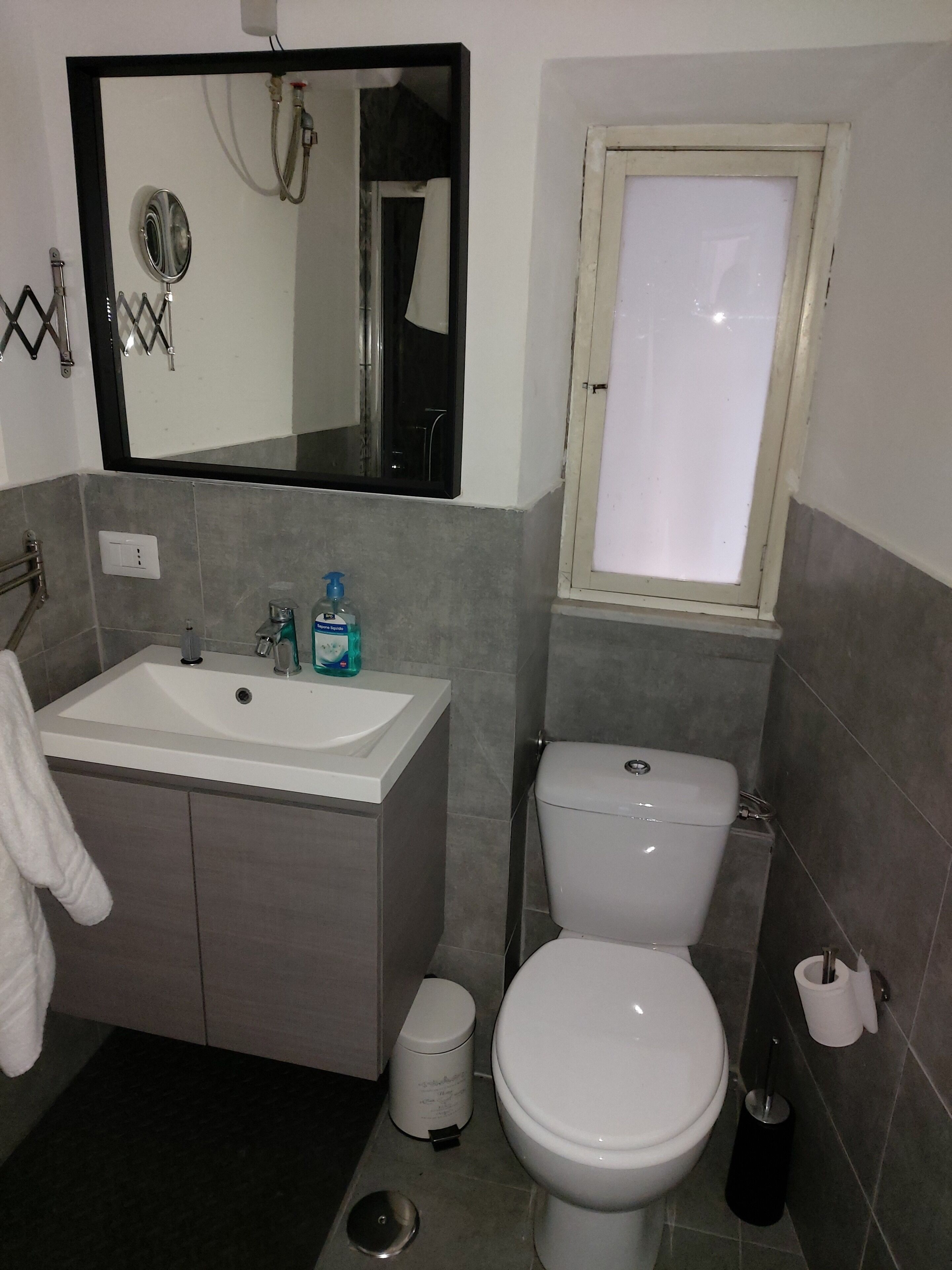 Un bagno con lavandino, specchio, WC e una finestra.