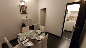 En matplats med ett runt bord för fyra personer, stolar, en liten växt och en inramad tavla på väggen.