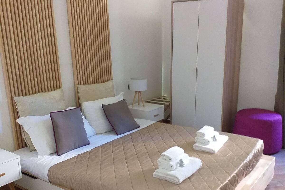 Ein modernes Hotelzimmer mit einem großen Bett, einem Kleiderschrank, einem Nachttisch und einem kleinen Tisch mit einer Lampe.