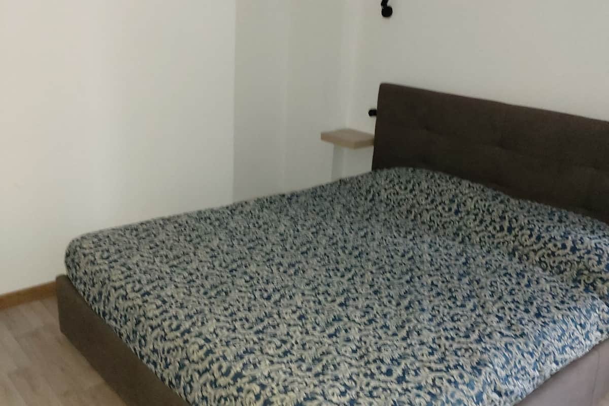 Ein Schlafzimmer mit einem Bett, einer Tür, einem kleinen Tisch und einer Wandleuchte.