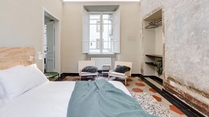 Ein Schlafzimmer mit einem Bett, zwei Stühlen, einem Fenster und einer Heizung.