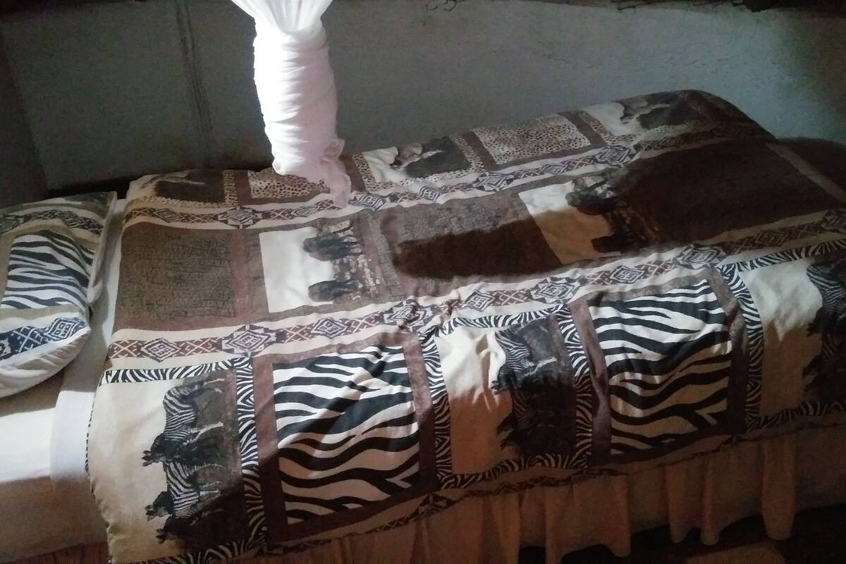 Una cama con una manta y almohadas estampadas con motivos de cebra, cabecera blanca y pared con textura.