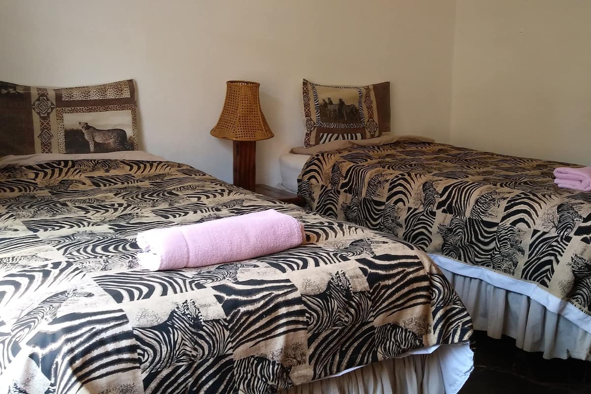 Dos camas individuales con ropa de cama a rayas de cebra, una lámpara trenzada y adornos en la pared.