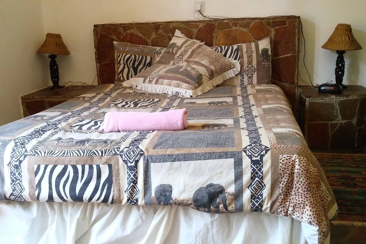 Una cama con una colcha estampada, dos mesitas de noche con lámparas y un cabecero de piedra.