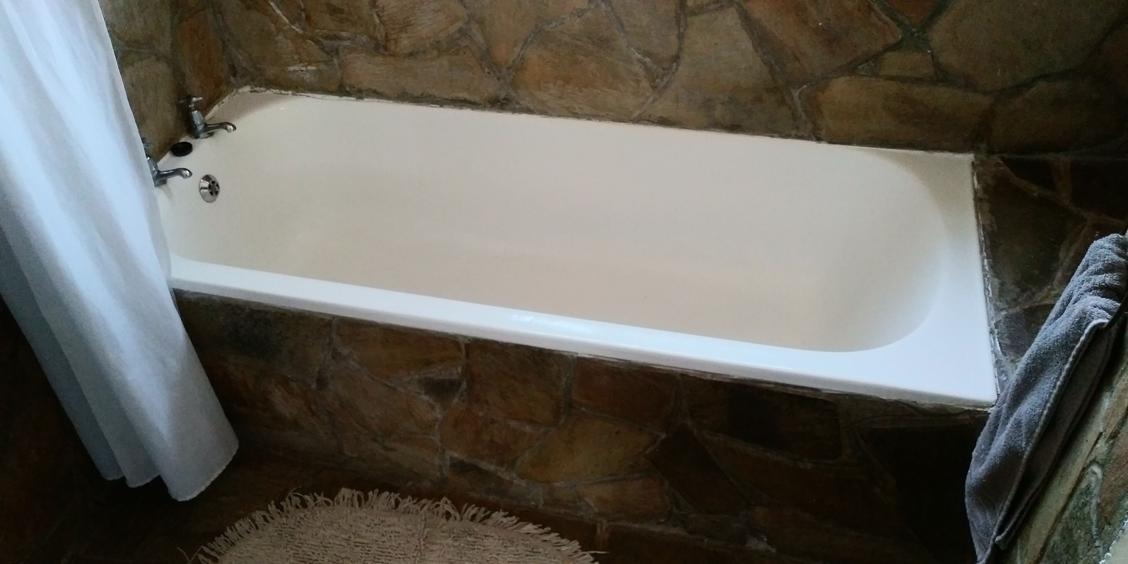 A bathroom with a stone wall, a bathtub, and a towel rack.