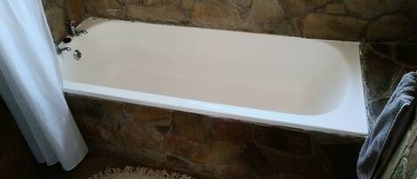 A bathroom with a stone wall, a bathtub, and a towel rack.