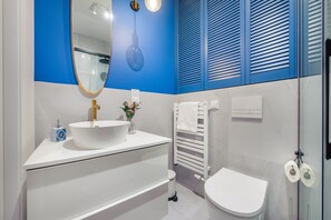Ein modernes Badezimmer mit einem weißen Waschbecken, einem Spiegel, einem Handtuchhalter und einer Toilette.