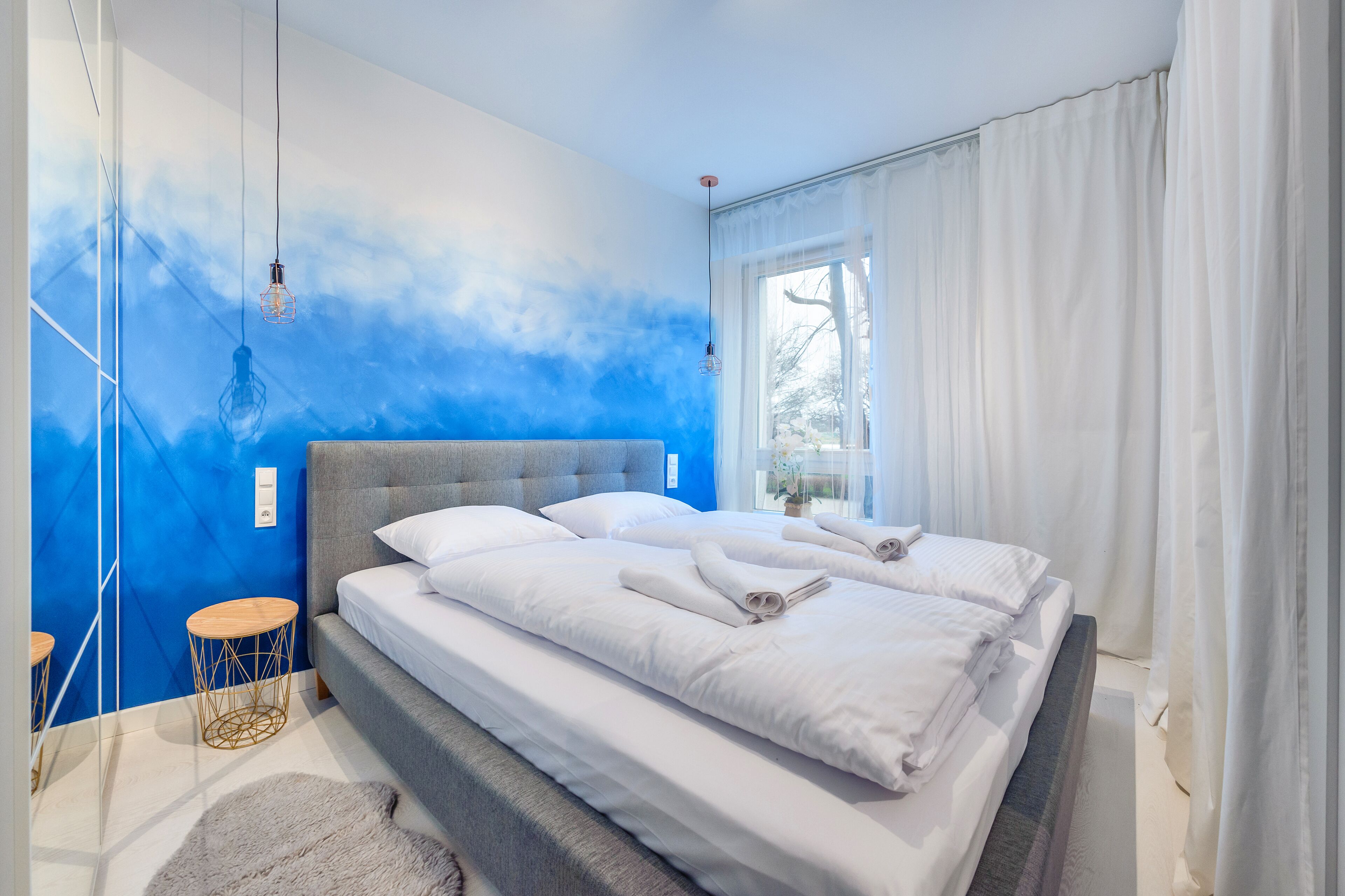 Une chambre moderne avec un grand lit, une tête de lit grise et un mur d’accent bleu.