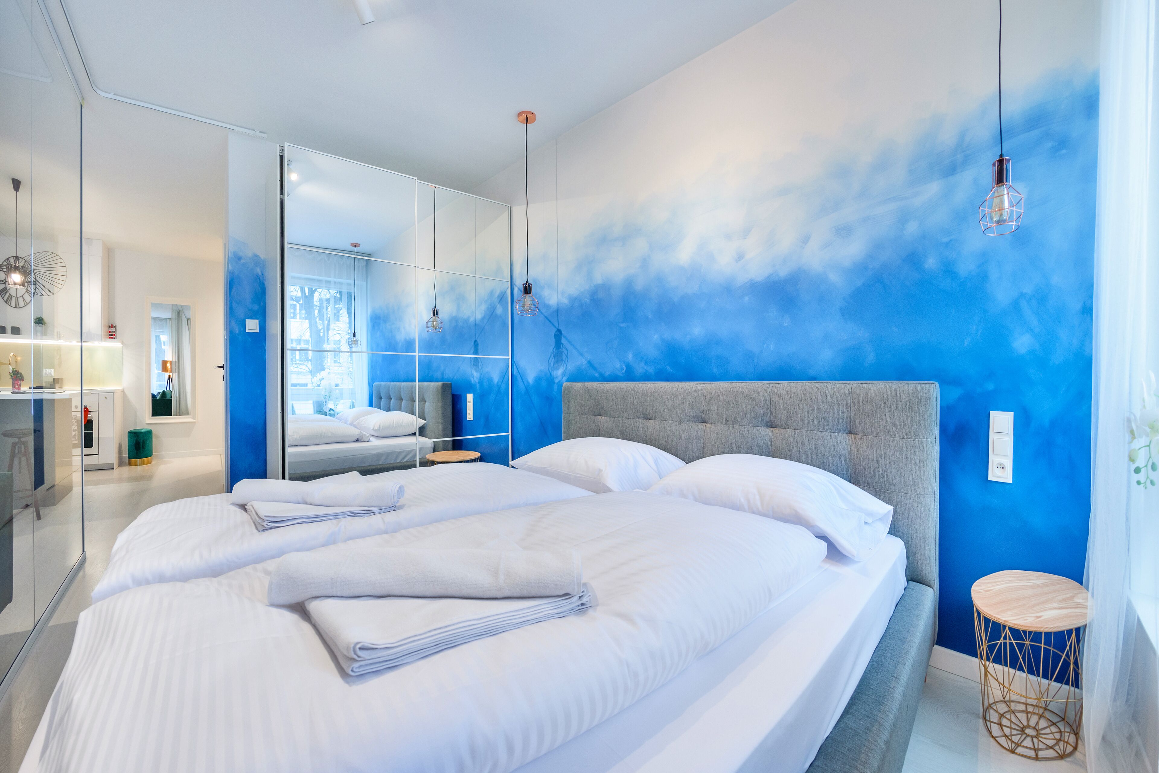 Una camera d'albergo moderna con un letto grande, un comodino, uno specchio e una parete decorata in blu.
