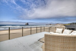 A beach view with a wooden deck, a wicker sofa, and a railing.