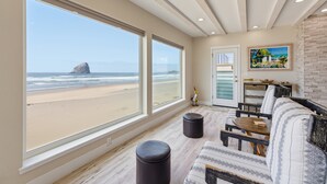 Ein Zimmer mit großen Fenstern mit Blick auf einen Strand, ein Sofa, ein kleiner Tisch und ein Gemälde an der Wand.