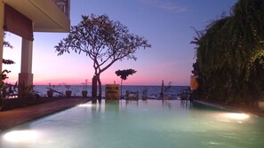 Une piscine à débordement offrant une vue sur l’océan au coucher du soleil.