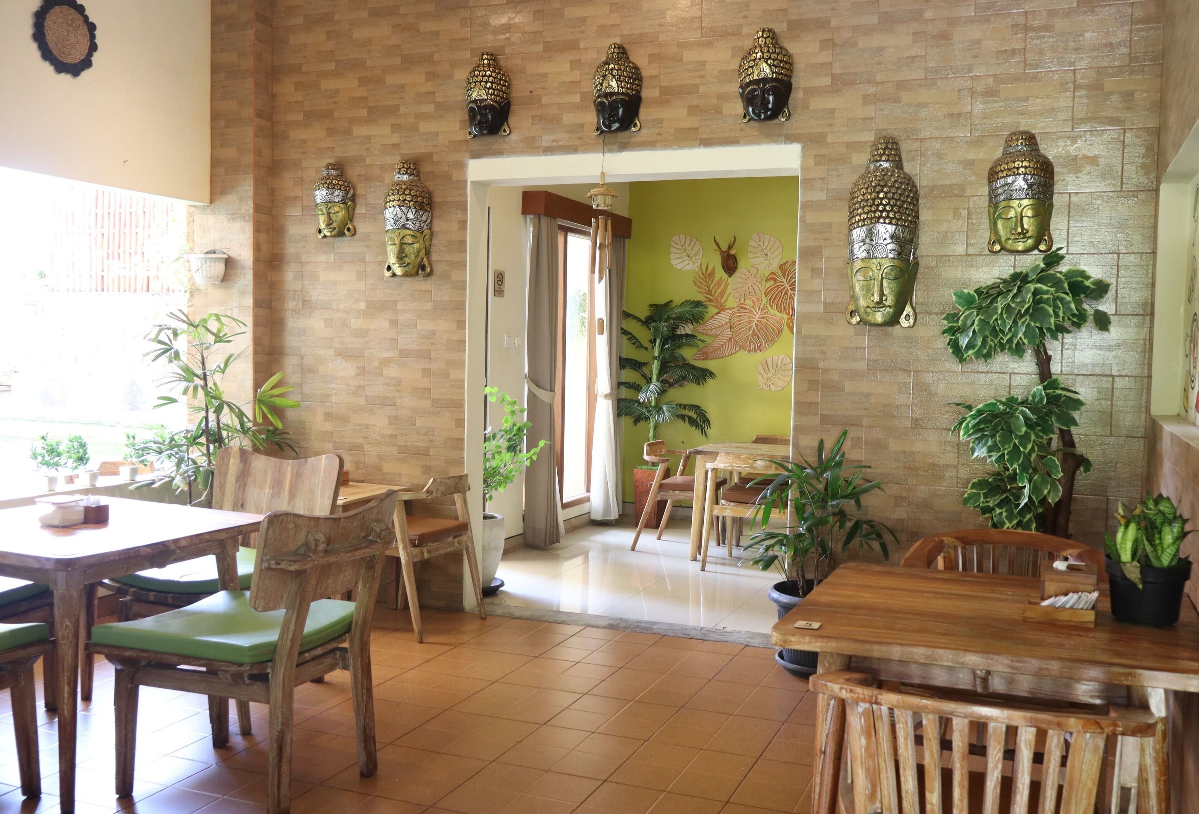 Un restaurante con muebles de madera, sillas con cojines verdes y estatuas decorativas de Buda en la pared.