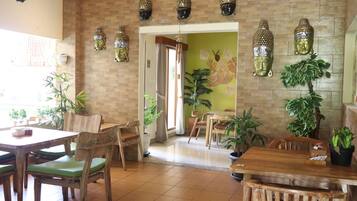 Un restaurante con muebles de madera, sillas con cojines verdes y estatuas decorativas de Buda en la pared.
