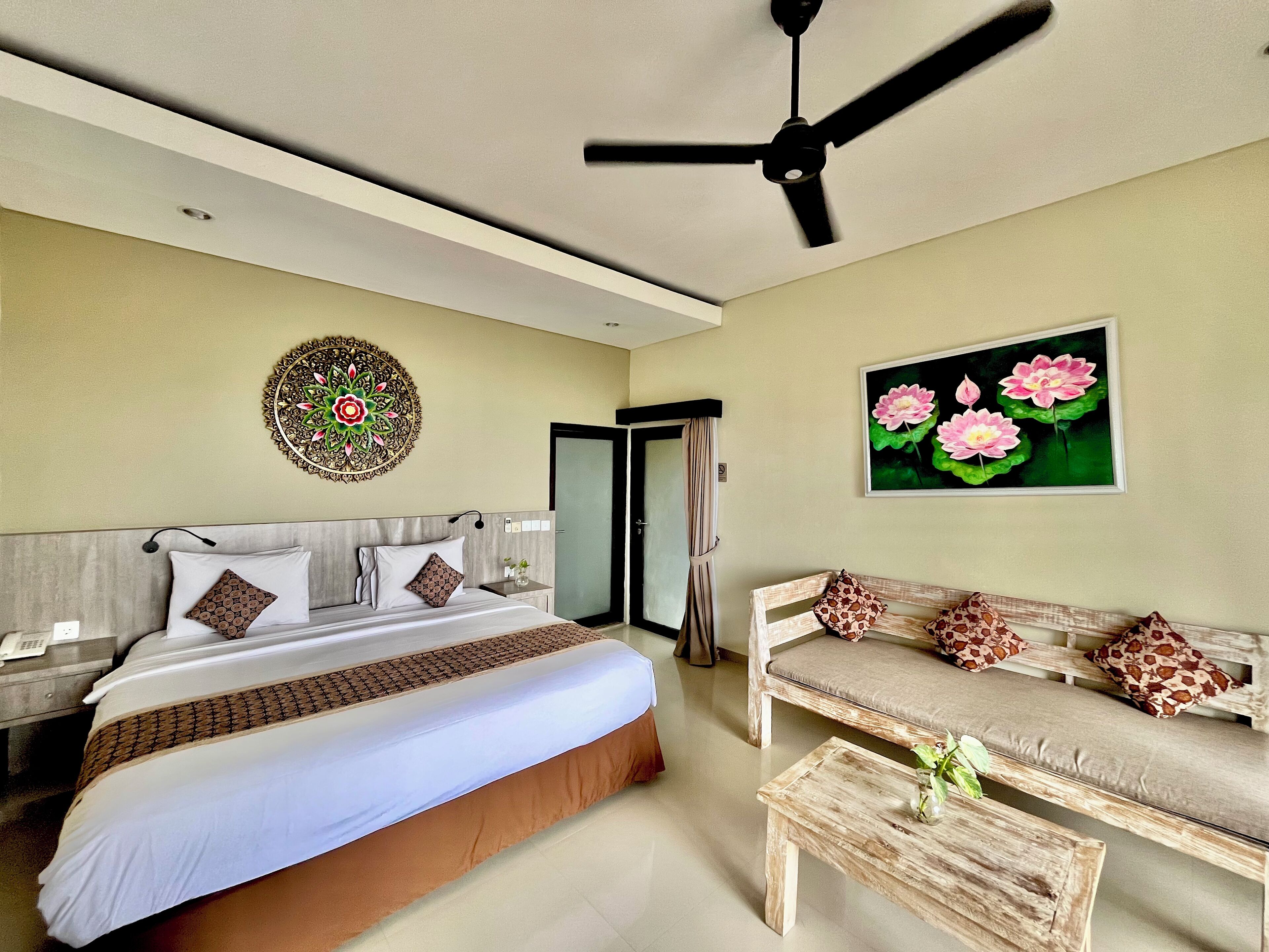 A hotel room with a bed, a sofa, a wooden coffee table, a ceiling fan, a wall-mounted decorative item, and a door.