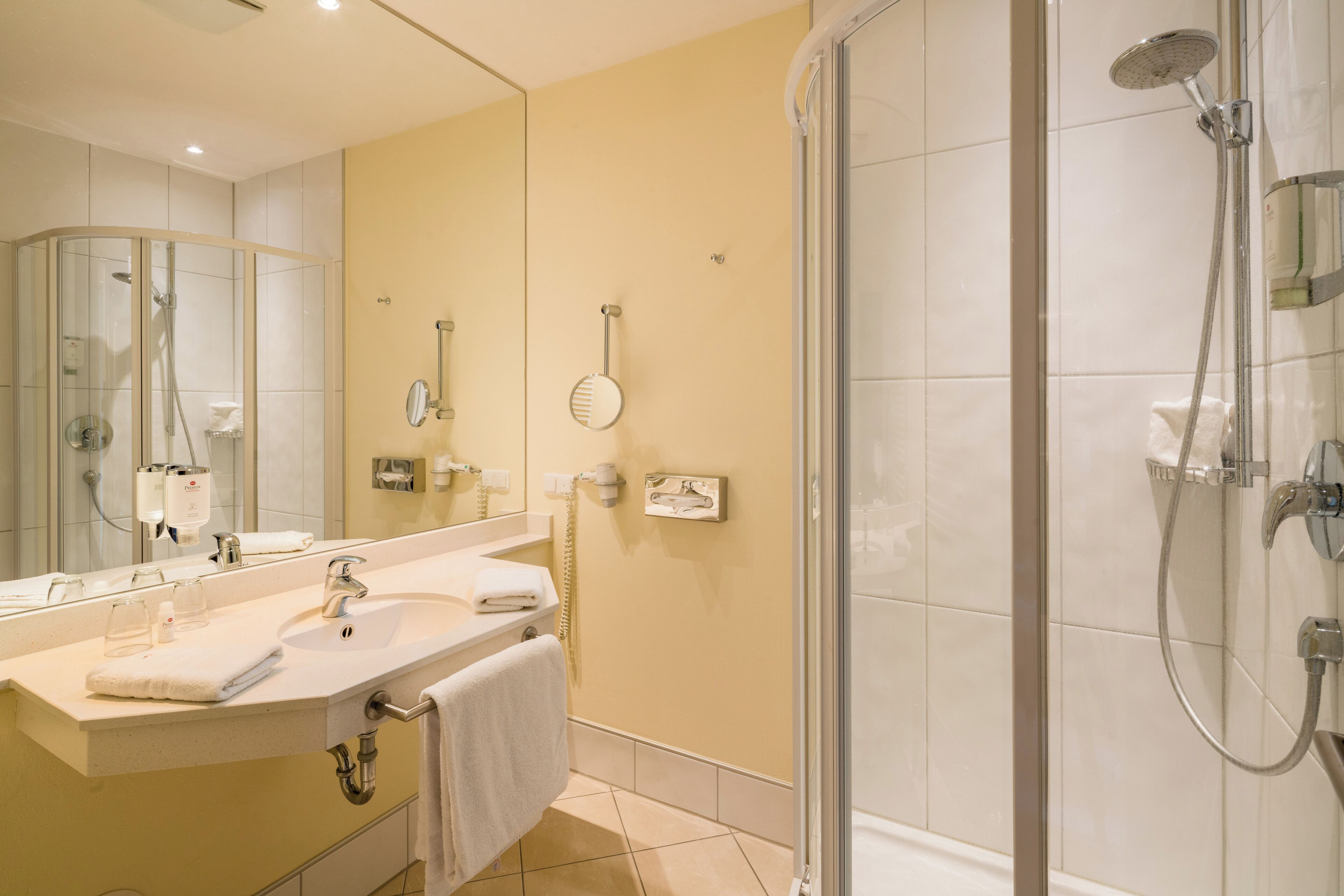 A modern bathroom with a glass-enclosed shower, a large mirror, and a vanity with a sink and towel rack.
