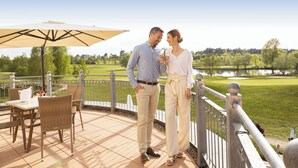 A couple standing on a deck with a view of a golf course and lake. - Castello Apartments (Adendorf)