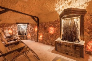 Una habitación con paredes de piedra, una chimenea, un sillón y una mesita.