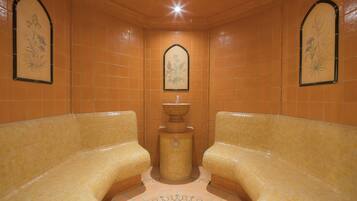 Ein Spa-Raum mit zwei gepolsterten Sitzbereichen, einer zentralen Fontäne und dekorativen Wandfliesen.
