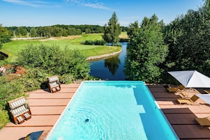 A swimming pool with lounge chairs and a view of a golf course and river.