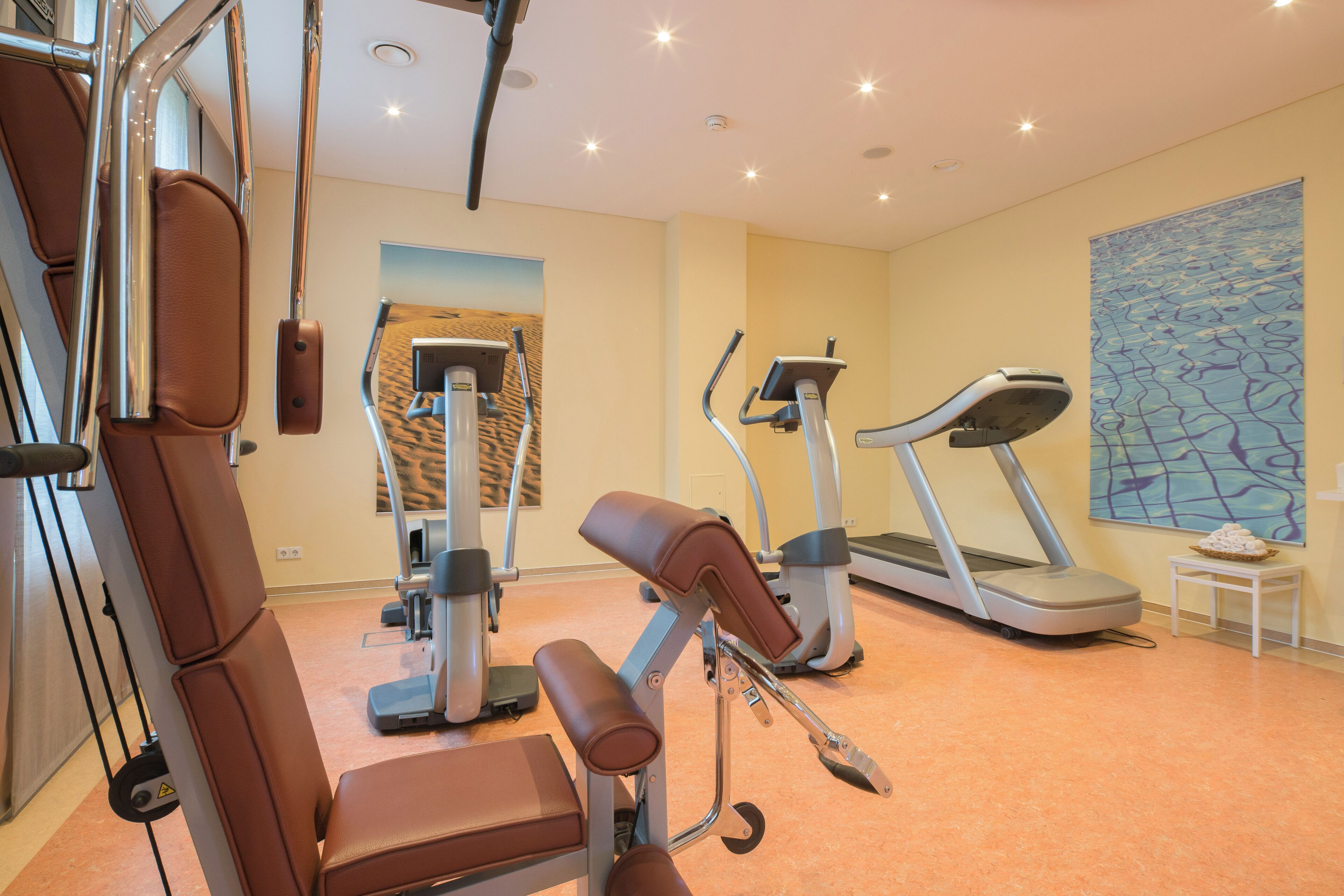 Ein Fitnessraum mit Trainingsgeräten, Laufband und einem Wandbild.