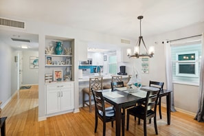 Uma cozinha moderna com armários brancos, um espaço de refeições com mesa e cadeiras de madeira e vista para a sala de estar adjacente.