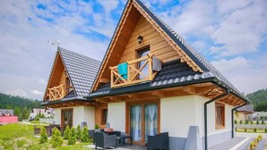 A wooden cabin with a balcony, a covered patio, and a garden area.