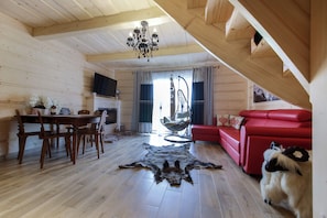 A wooden interior with a dining table, chairs, a red sofa, a chandelier, and a dog. - Domki Dream House Jędruś (Poronin)