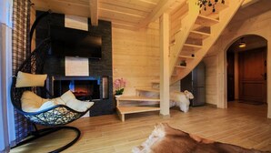 A cozy interior with a wooden staircase, a hanging chair, a fireplace, and a dog lying on the floor.