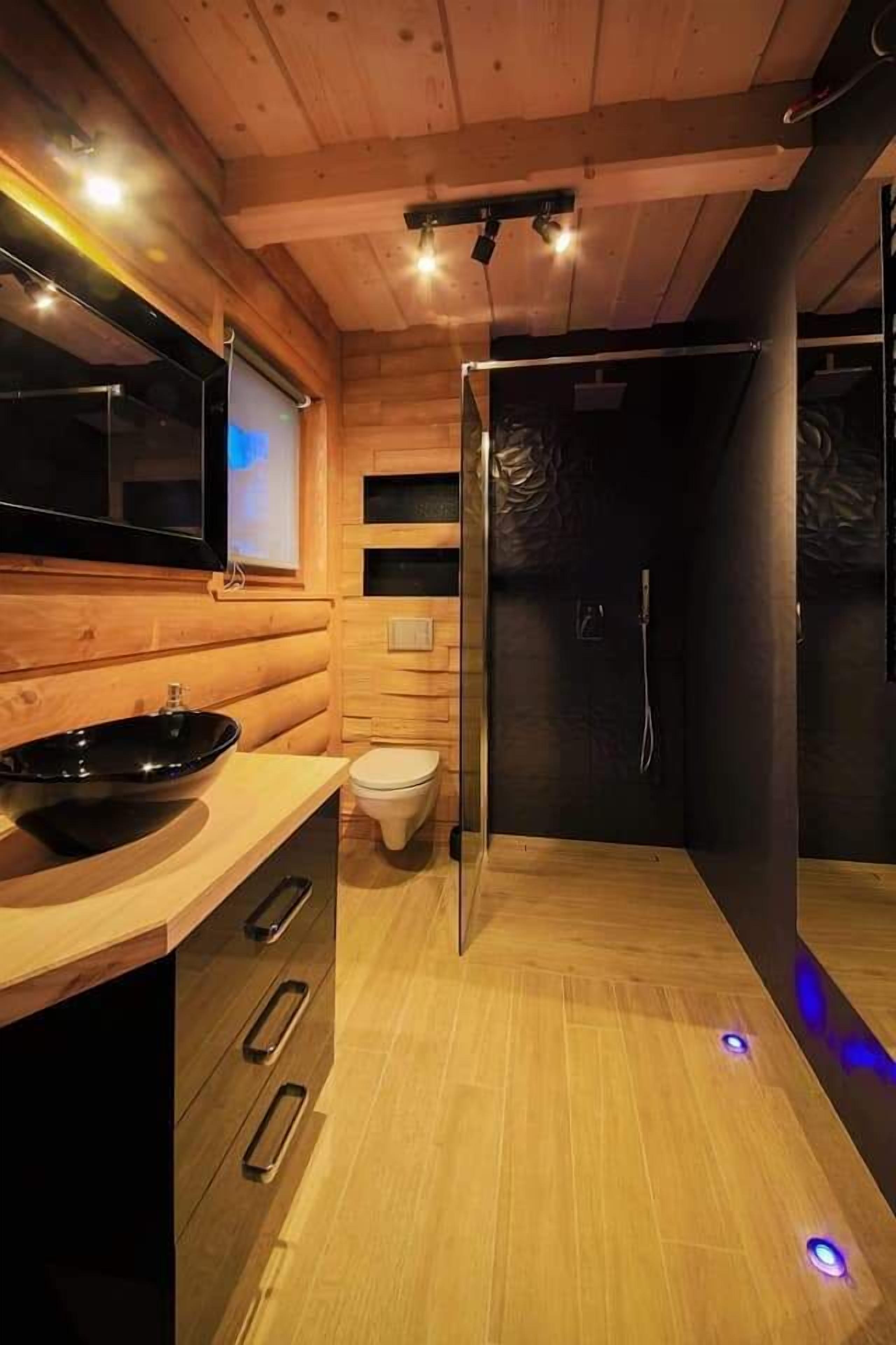 A modern bathroom with a wooden interior, a black sink, a toilet, and a shower area.