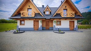 A two-story wooden house with a symmetrical facade, two balconies, and a gravel driveway.