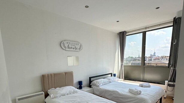 Et hotelværelse med to senge, en radiator, et vindue med gardiner og et skilt med teksten 'Welcome to our home'.