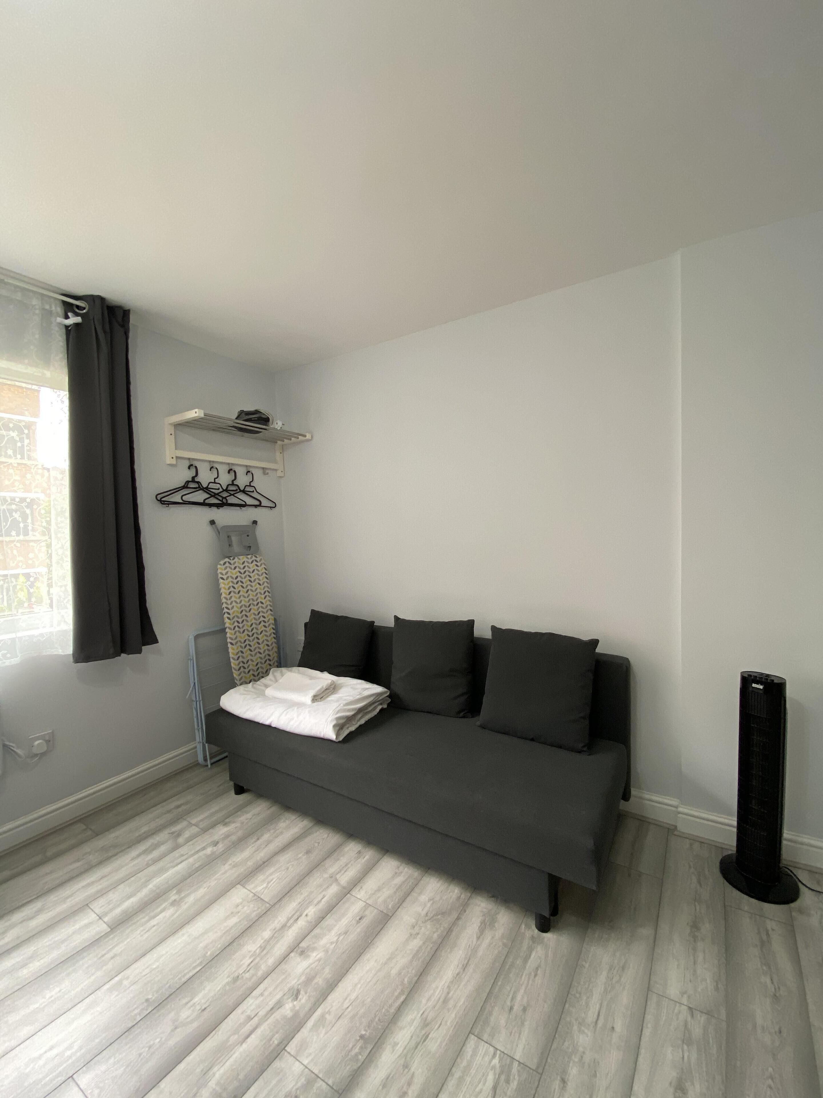 Una habitación moderna y minimalista con un sofá gris, una plancha pequeña, un radiador y un calentador portátil.