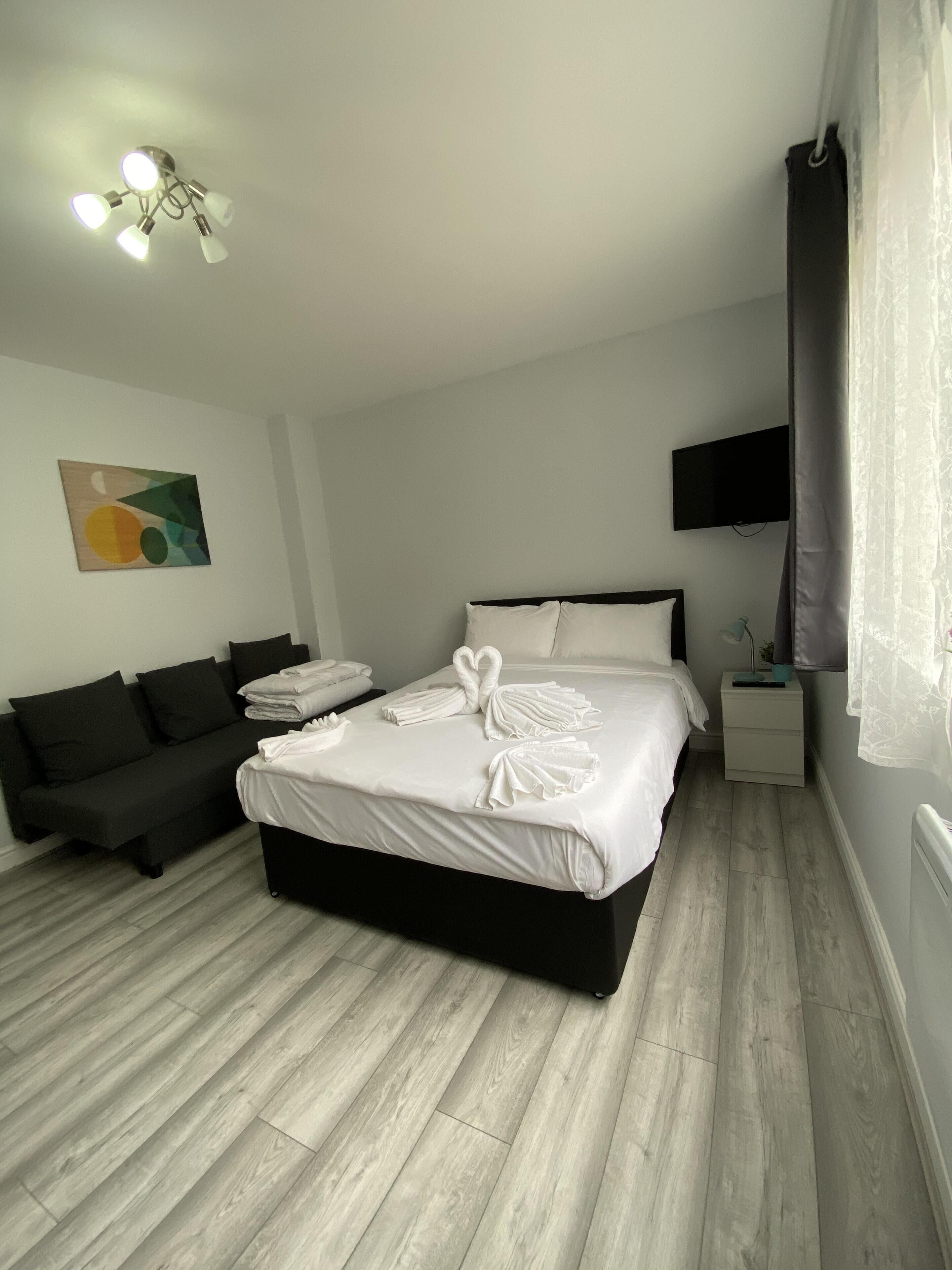 A modern hotel room with a large bed, a sofa, a flat-screen TV, and a ceiling light fixture.