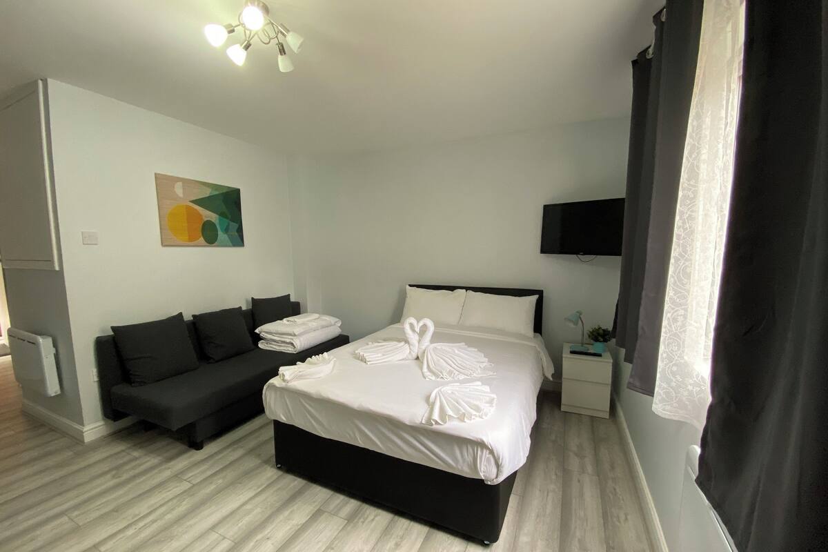 A hotel room with a large bed, a sofa, a flat-screen TV, and a painting on the wall.